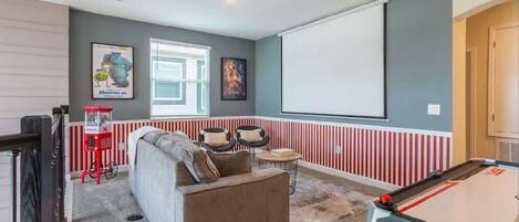 A room with a pool table, a sofa, and a projector screen.