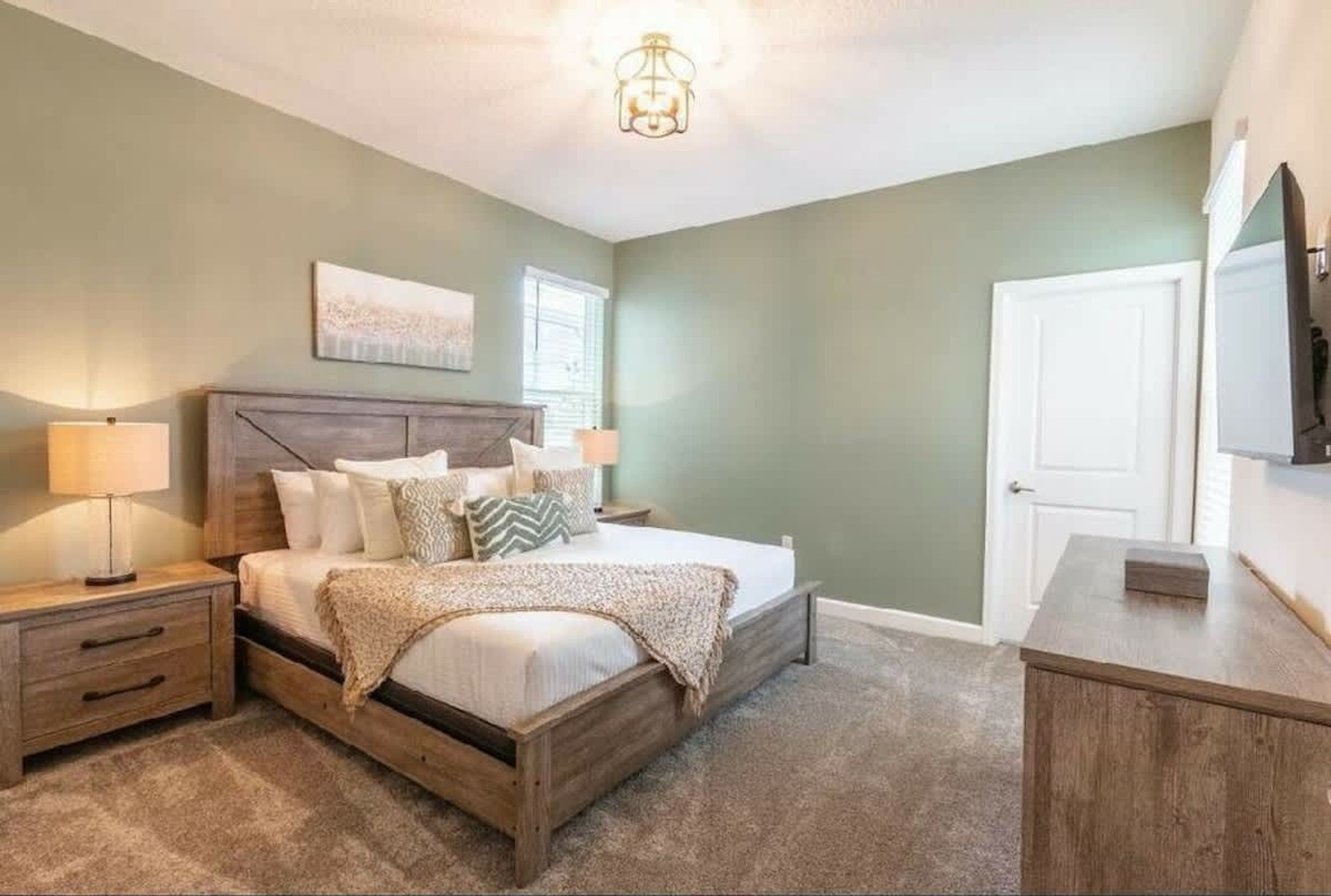 A bedroom with a wooden bed, two bedside tables, a nightstand, a wall-mounted TV, and a door.