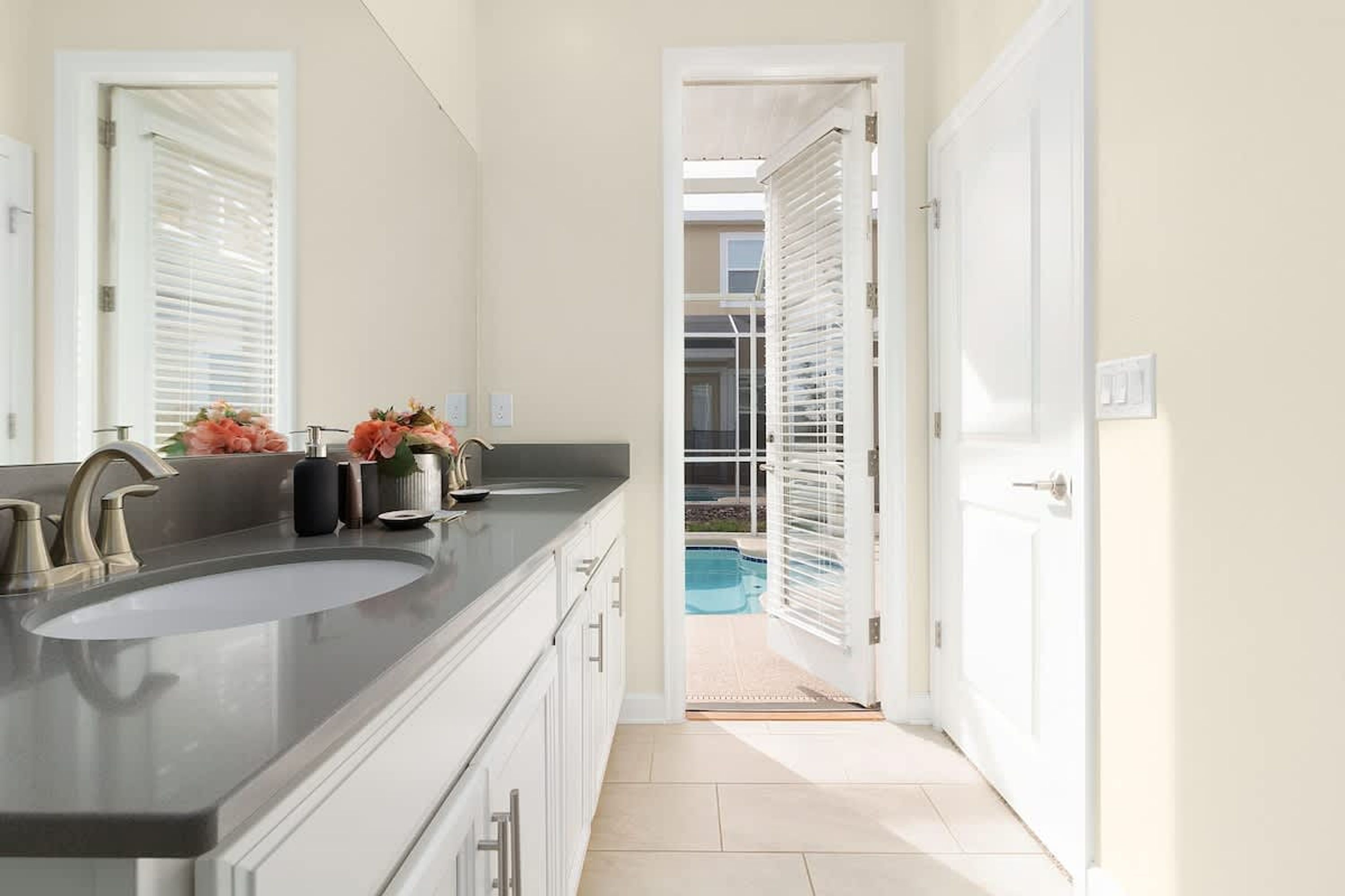 A modern bathroom with a large sink, two mirrors, and a view of a pool through an open door.