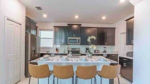 A modern kitchen with dark cabinets, a central island with bar stools, and a large window providing natural light. - Toy Story Villa - 5BD Game Room Pool Spa Near Disney (Davenport)