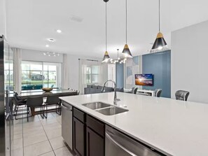 A modern kitchen with a large island, pendant lights, and a dining area with a view of the outdoors. - Super Huge- 12bd 12bas - Sleeps 38 (Kissimmee)