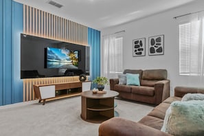 A modern living room with a flat-screen TV, a brown sofa, a coffee table, and a blue accent wall. - Super Giant - 12bd 12bas - Sleep 38 Near Disney (Kissimmee)