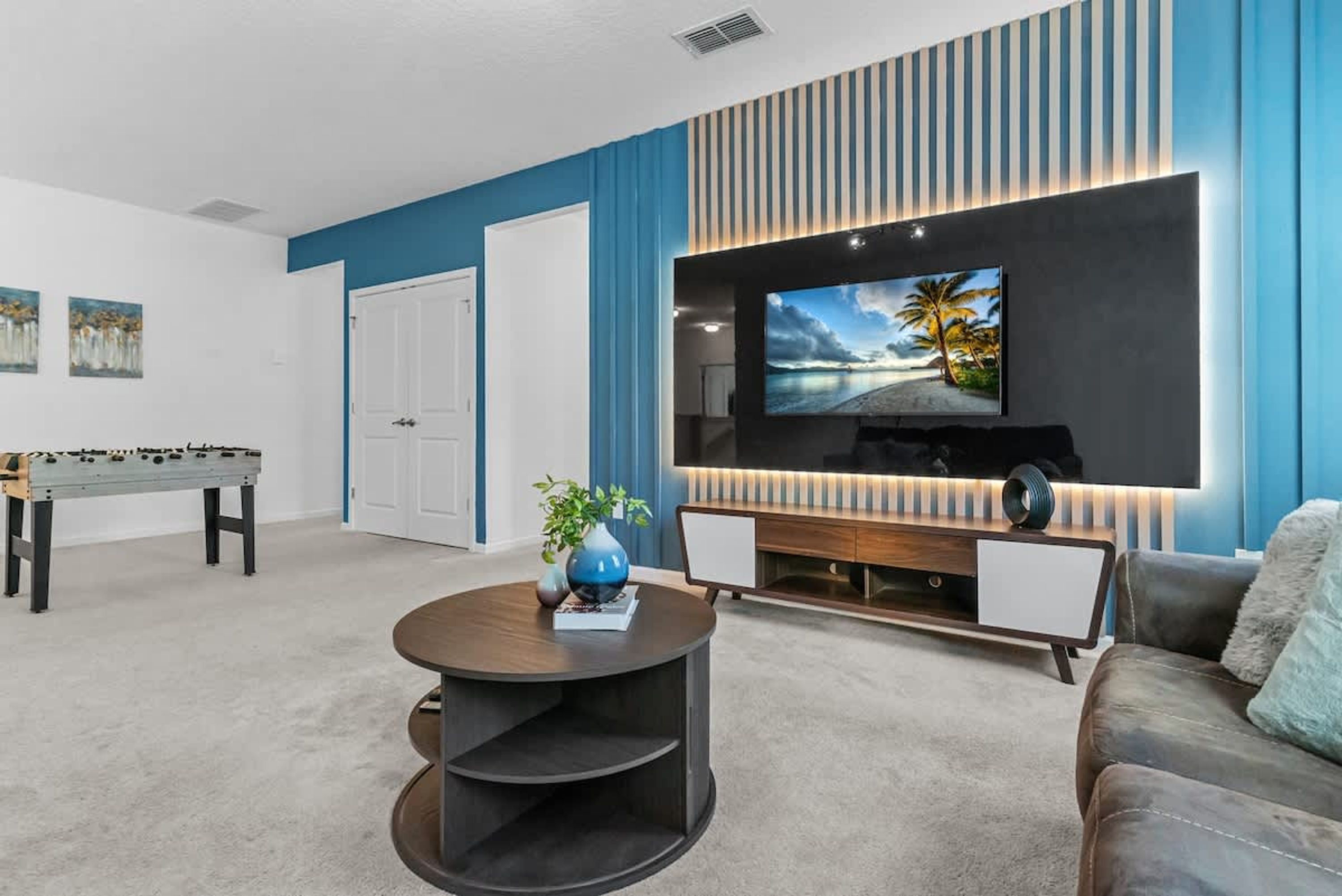 Ein modernes Wohnzimmer mit einem großen Flachbildfernseher an der Wand, einem runden Couchtisch, einer Couch und einem Kicker.