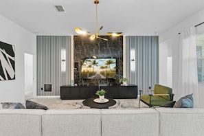 Una sala de estar moderna con un televisor grande, un mueble de entretenimiento negro, un sillón verde y una pared decorativa de mármol.