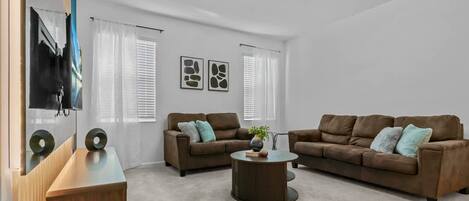 A modern living room with two brown sofas, a wooden coffee table, and a TV on a stand.