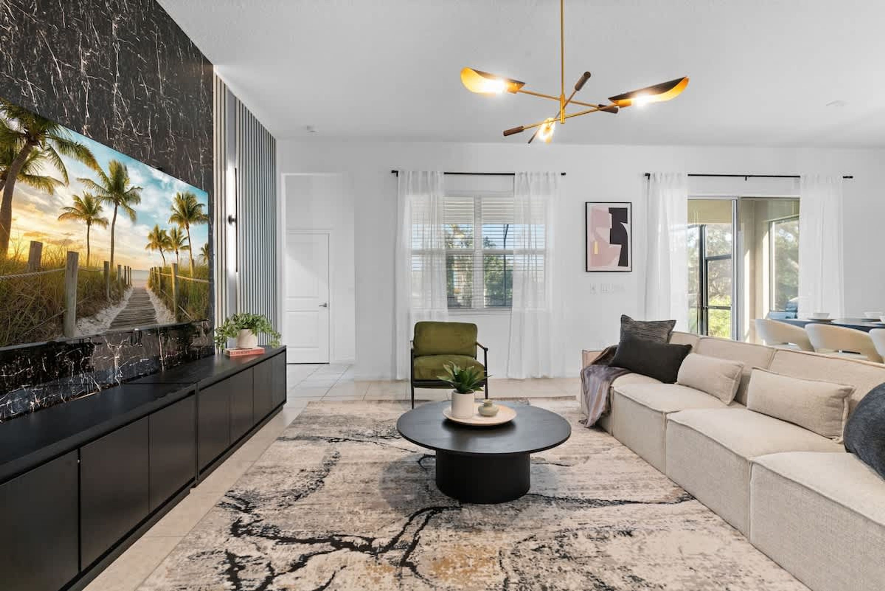 Un salon moderne avec un mur en marbre noir, un grand tableau représentant un coucher de soleil, une table basse ronde, un canapé beige et un fauteuil vert.