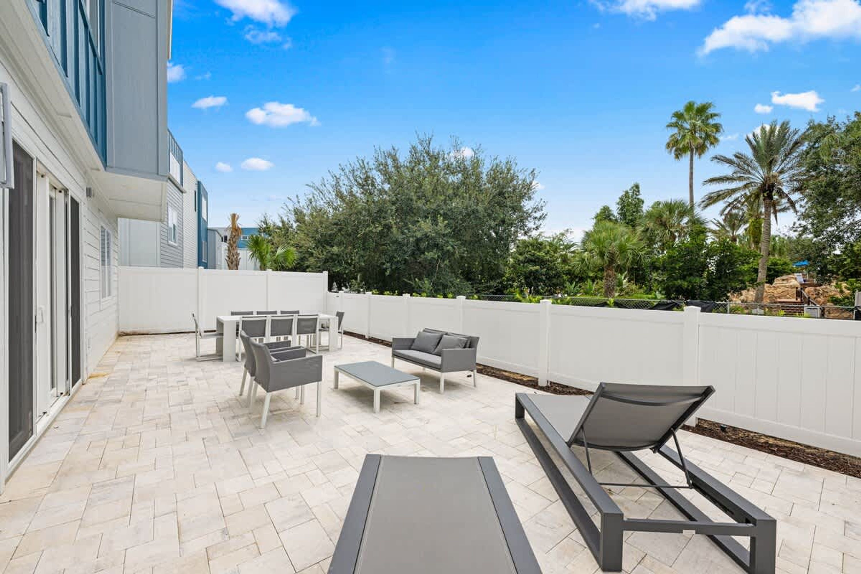 A patio with outdoor furniture, a white fence, and lush greenery.