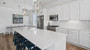 A modern kitchen with white cabinetry, stainless steel appliances, and a large island with bar stools. - Modern Family 7BR w Private Pool and Patio (Miramar Beach)