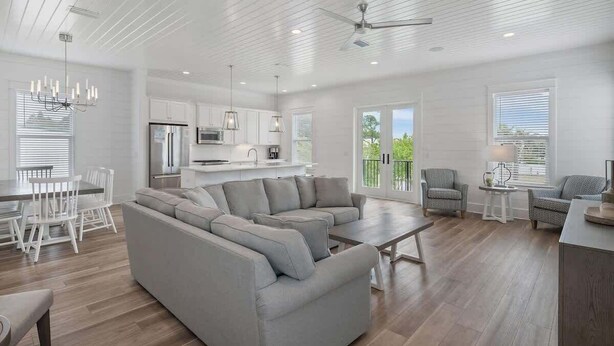 A spacious living room with a sectional sofa, a dining area with white chairs, a kitchen with white cabinets, and a ceiling fan. - Modern Family 7BR w Private Pool and Patio (Miramar Beach)
