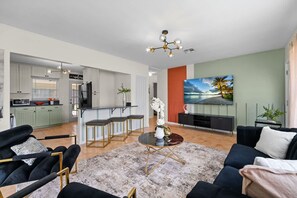 A modern living room with a black sofa, a glass coffee table, and a painting of a beach scene. - Lake Toho Parks Pool Fishing Sleeps 8 (Kissimmee)