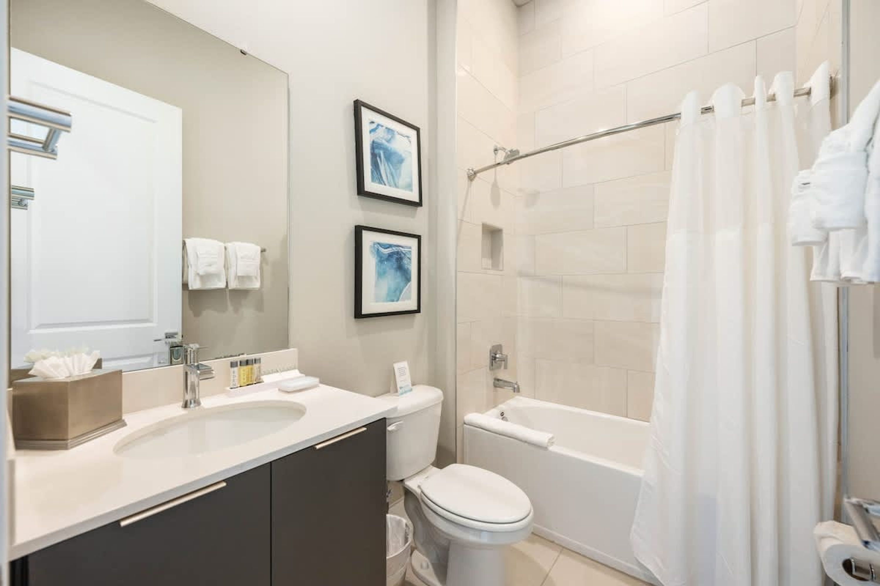 A modern bathroom with a double sink, toilet, bathtub, and a shower curtain.