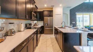 A modern kitchen with dark cabinetry, stainless steel appliances, and a large island. - Pool Spa Arcade Games - 5 min Walk to Water Park (Kissimmee)