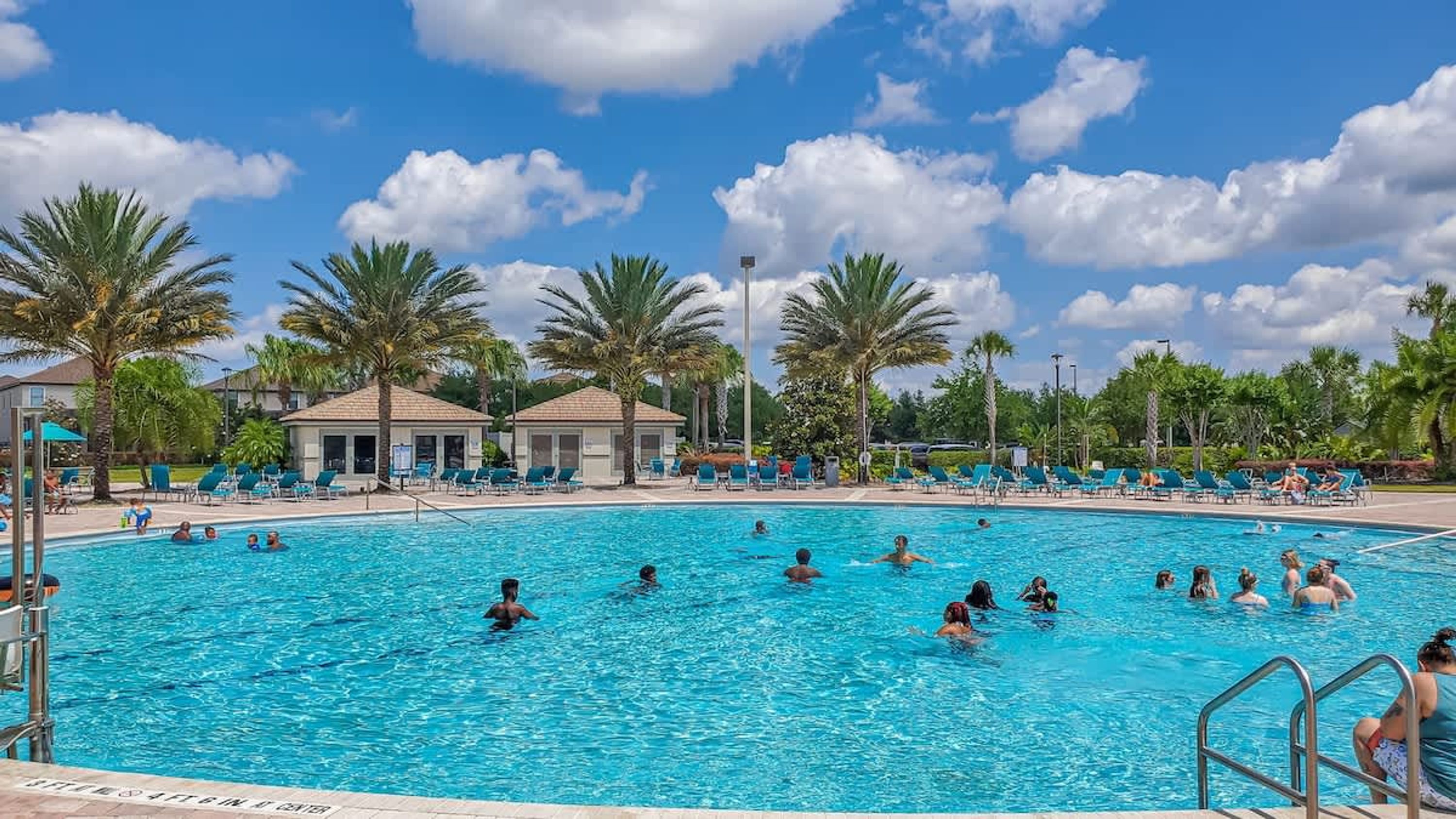 Uma grande piscina ao ar livre rodeada por palmeiras e espreguiçadeiras.