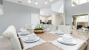 A spacious dining area with a long wooden table set for six, white upholstered chairs, and a central plant. - Ultimate Comfort Prime Location Luxury Villa (Kissimmee)