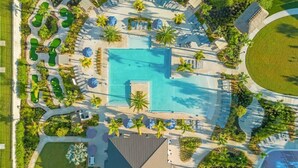 An aerial view of a resort with a central swimming pool, surrounded by lounge areas and palm trees. - Ultimate Comfort Prime Location Luxury Villa (Kissimmee)