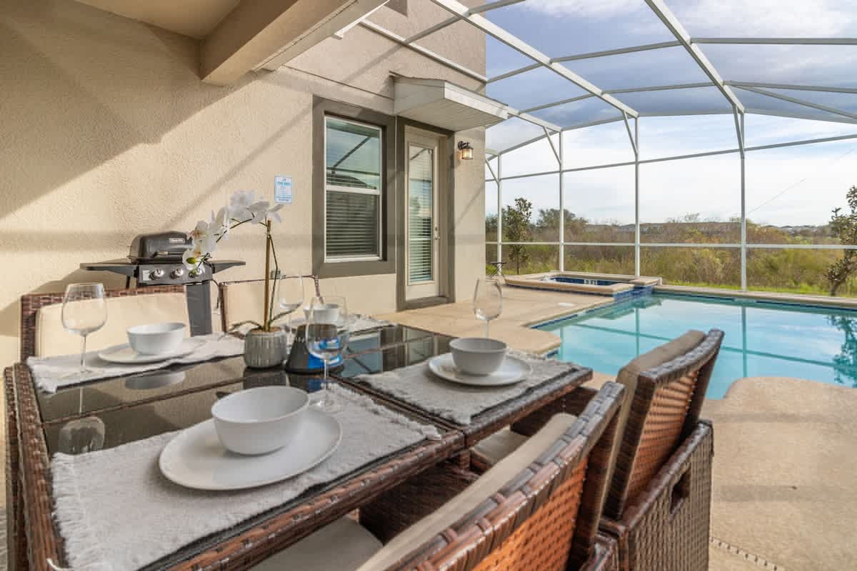 Zona de comedor junto a la piscina con una mesa para dos, una parrilla y vistas a la piscina y al paisaje.
