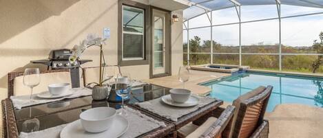 Zona de comedor junto a la piscina con una mesa para dos, una parrilla y vistas a la piscina y al paisaje.