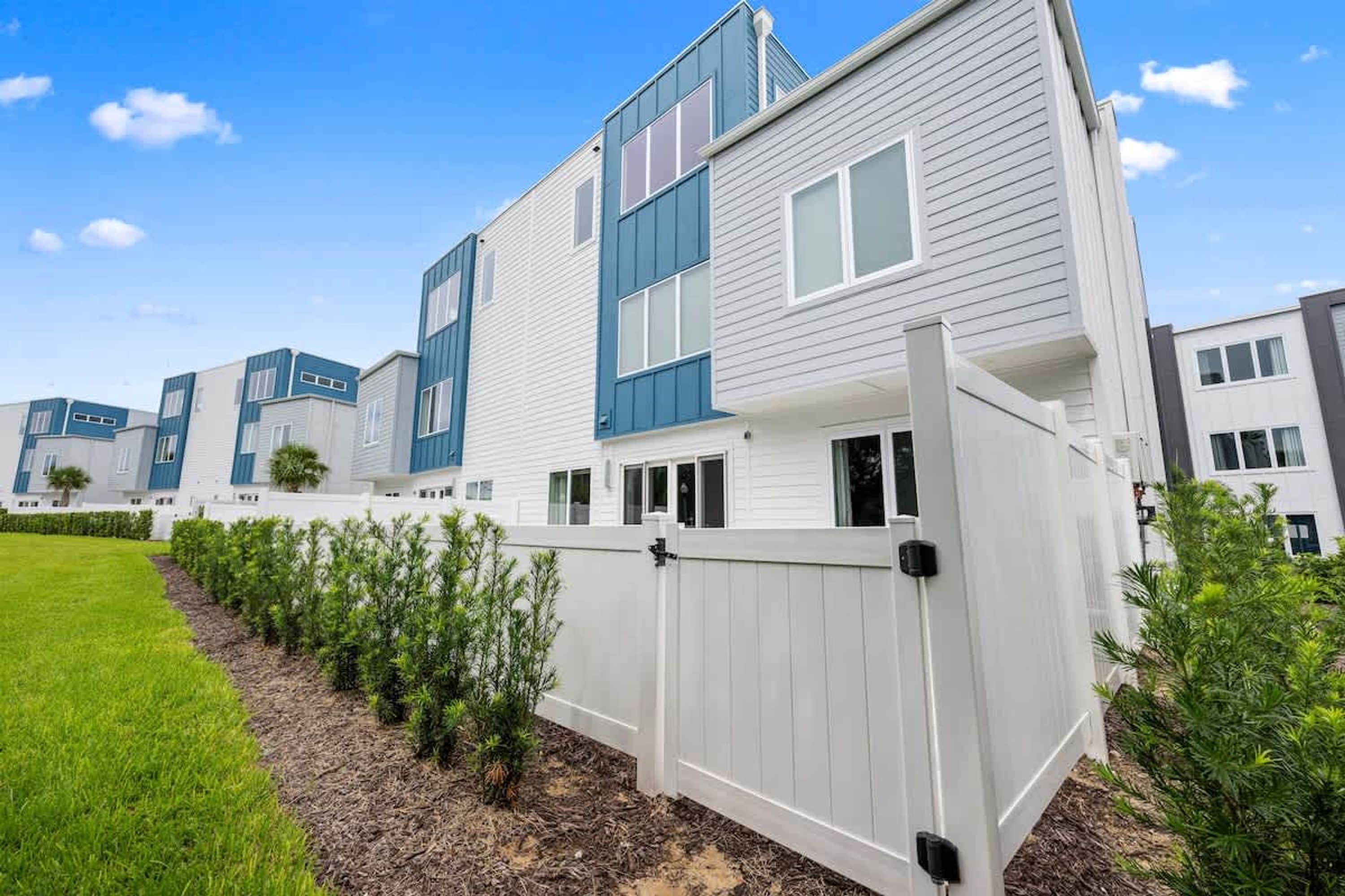 A modern residential building with a white exterior and blue accents, surrounded by a well-maintained lawn and small shrubs.