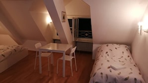 A small, cozy room with a single bed, a small table, and two chairs. There is a window with a view of the outside. - Room-studio D on Barfüsserplatz Central (Basel)