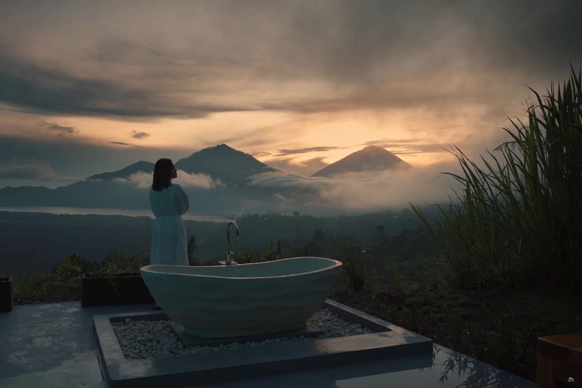 A person standing by a large bathtub with a view of mountains and clouds.