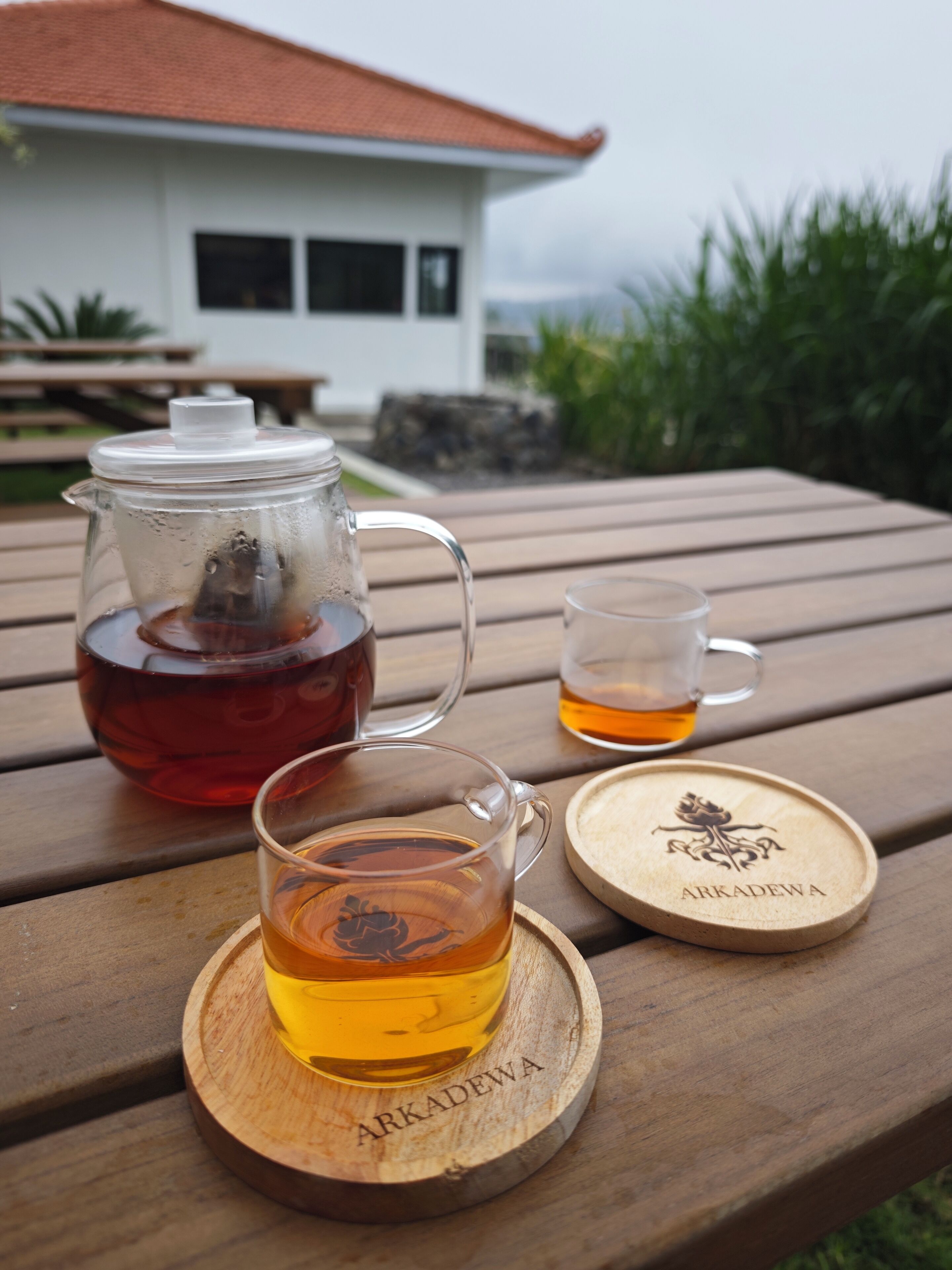 Ein Holztisch mit einem Teekessel, einer Tasse und einem Untersetzer mit dem Namen ARKADEWA.