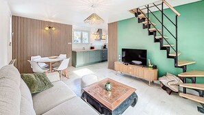 Una sala de estar moderna con un sofá, una mesa de centro y un televisor. Se ve una escalera con una pared verde y una cocina al fondo.