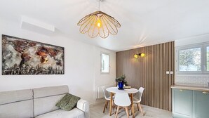 Una sala de estar moderna con un sofá gris, una mesa de comedor redonda con sillas blancas, una lámpara colgante y un mapa del mundo en la pared.