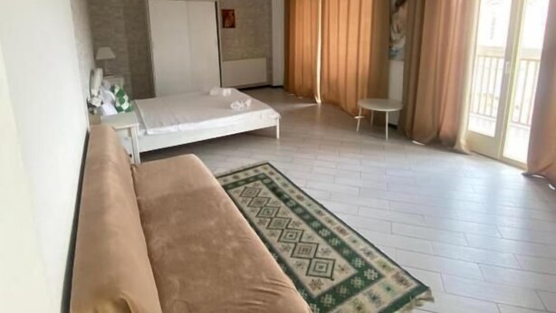 A spacious bedroom with a bed, a bench, a small table, and a window with curtains. - Boutique Hotel Meidan View (Tbilisi)