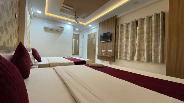 A hotel room with two beds, a ceiling fan, an air conditioning unit, a TV mounted on the wall, and a window with curtains. - LOTO HOTEL MAHAKAL Ujjain Tower Chowk (Ujjain)
