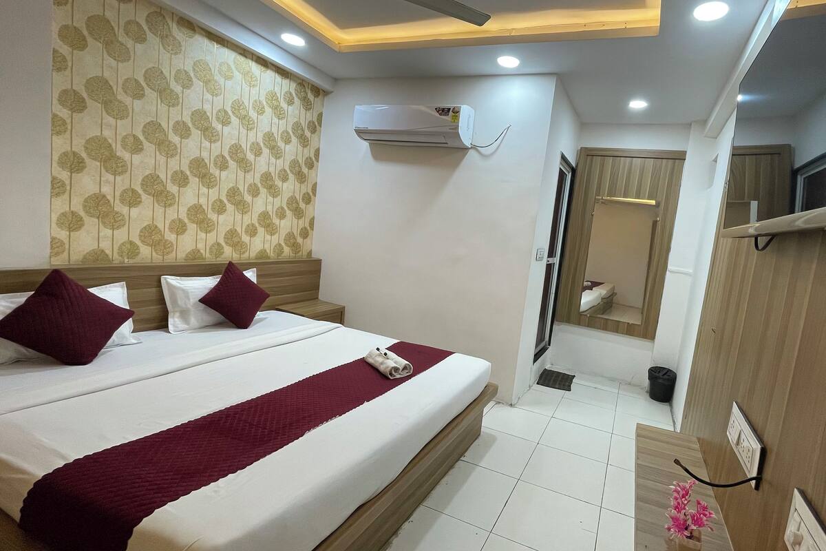 Una camera d'albergo con un letto grande, un comodino, un condizionatore d'aria, uno specchio e un bagno piccolo con il water e il lavandino.