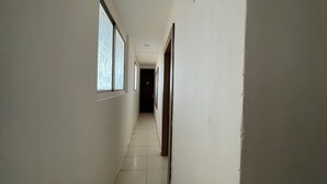 A narrow hallway with white walls and tiled flooring, leading to a dark door at the end. - LOTO HOTEL MAHAKAL Ujjain Tower Chowk (Ujjain)