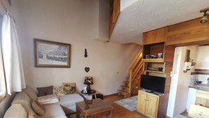Una sala de estar acogedora con un sofá, una mesa de centro, un televisor y una escalera que lleva a una cocina.
