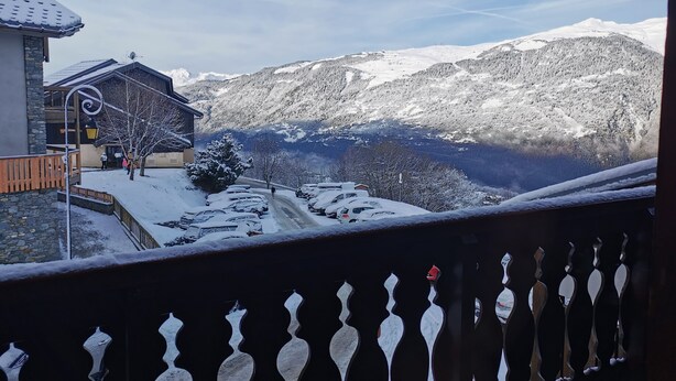 Paisaje nevado de montañas con un edificio que tiene un balcón y una valla de madera.