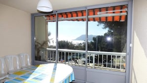 A balcony with a view of the sea and mountains, a table with a striped tablecloth, and white plastic chairs. - Apartment in Pin Rolland by Ste Asile Beach (Saint-Mandrier-sur-Mer)