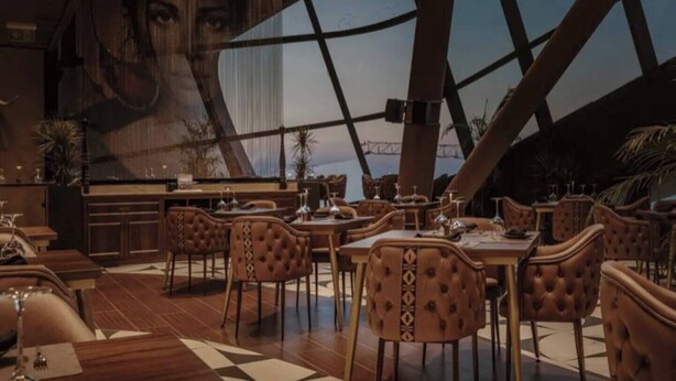 Un restaurante con techos altos y un amplio ventanal con vistas a un paisaje urbano.