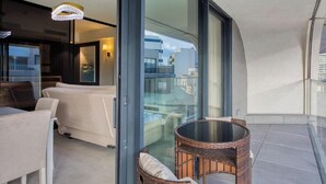 Una sala de estar moderna con un sofá, una mesa redonda de mimbre y una puerta de cristal que da a un balcón.
