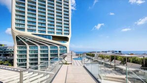 Un hotel moderno con fachada de vidrio curvada, piscina en la azotea y vistas al mar.