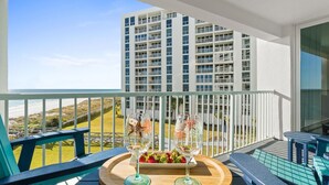 Varanda com uma mesa posta para dois, com vista para a praia e um edifício alto.