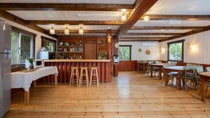 Habitació espaiosa amb terres de fusta, una zona de bar central amb tamborets i diverses taules i cadires.