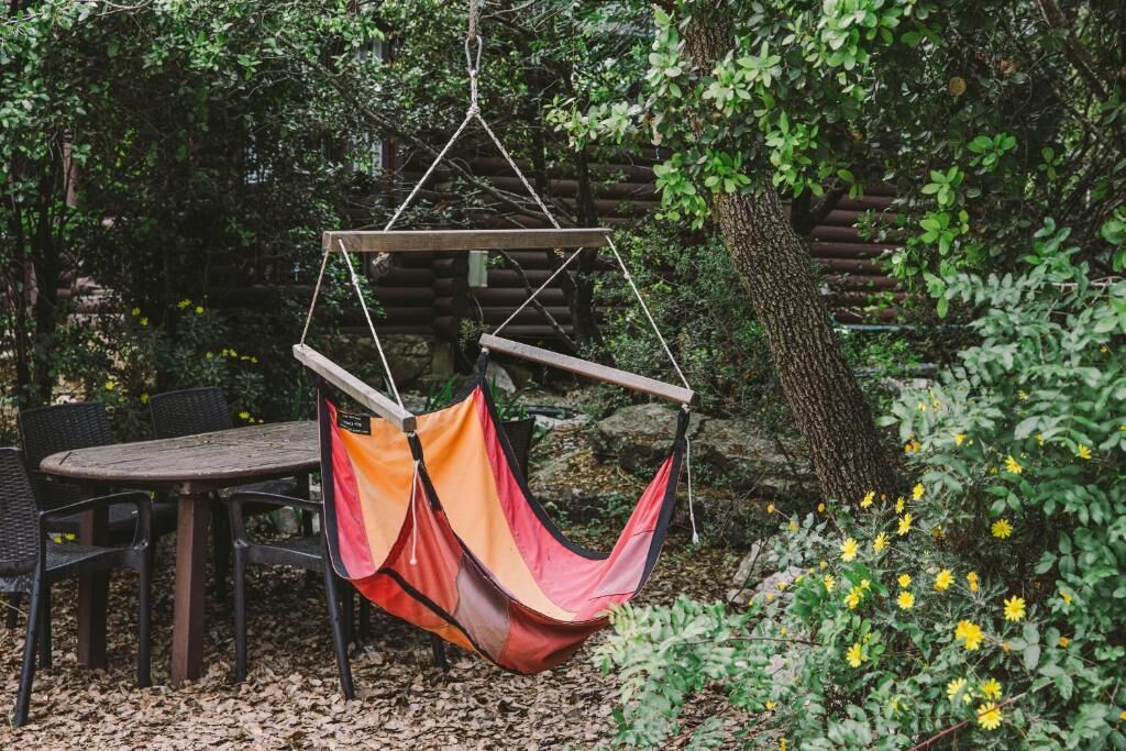 Eine Hängestuhl-Sitzgelegenheit, befestigt an einer Holzkonstruktion in einem Garten mit einem Tisch und Stühlen in der Nähe.