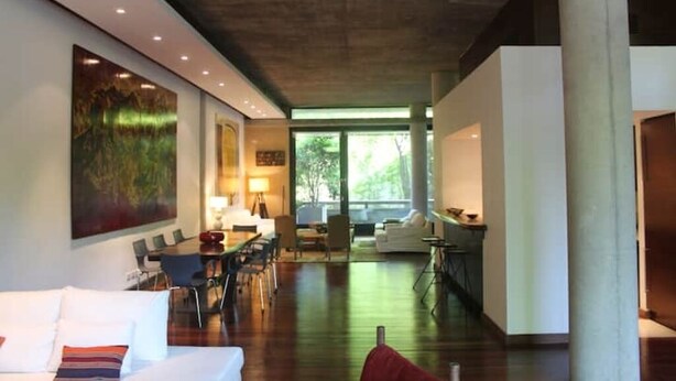 Een ruime woonkamer met een eettafel, banken en een groot raam dat voor natuurlijk licht zorgt.
