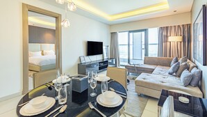 A modern hotel room with a dining area, a sofa, a TV, and a large window. - Superhost 1BR DAMAC Towers Paramount (Dubai)