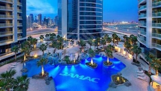 A modern hotel with a central pool area, surrounded by palm trees and a city skyline in the background. - Superhost 1BR DAMAC Towers Paramount (Dubai)