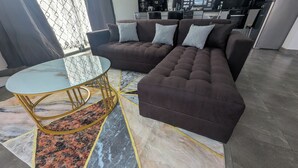 A modern living room with a sectional sofa, a glass-top coffee table, and a patterned rug.