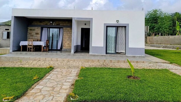 A modern two-story house with a patio, a dining area with a table and chairs, and a small garden.