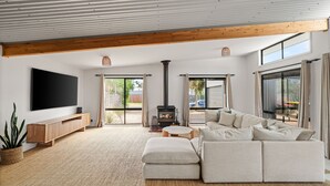 A spacious living room with a large sectional sofa, a flat-screen TV, a fireplace, and large windows offering views of the outdoors. - Woolamai Waters Retreat (Cape Woolamai)