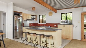 A modern kitchen with a central island, stainless steel appliances, wooden cabinets, and a large window providing natural light. - Woolamai Waters Retreat (Cape Woolamai)
