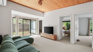 A modern living room with a large TV, green sofas, and a wooden ceiling. - Woolamai Waters Retreat (Cape Woolamai)