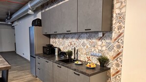 A modern kitchen with grey cabinets, a stainless steel refrigerator, a coffee maker, and a potted plant.