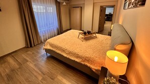 A bedroom with a large bed, a bedside table with a lamp, and a window with curtains.